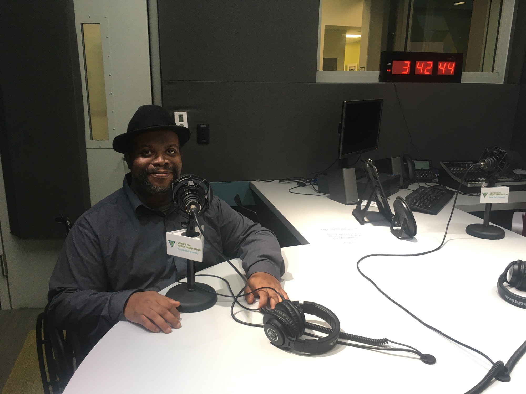 The main photo features David Hale, a black man wearing a fedora and a dark button down shirt. in front of a microphone in a podcast studio.